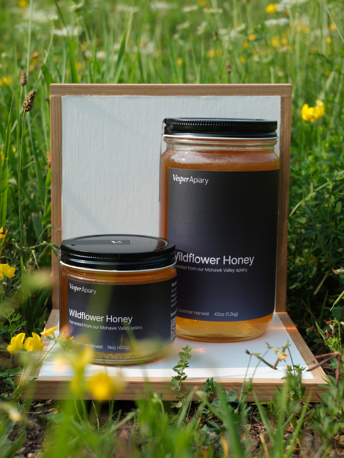 Two jars of Wildflower Honey from Vesper Apiary in a white display stand with a natural background